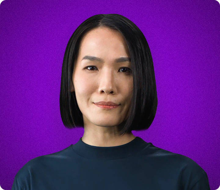 Actor Portrayal; A middle-aged woman, smiling slightly while looking directly straight-ahead, on a purple background.